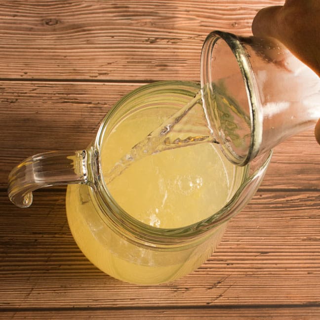 L'eau de la carafe est versée dans le pichet contenant le sirop de citron