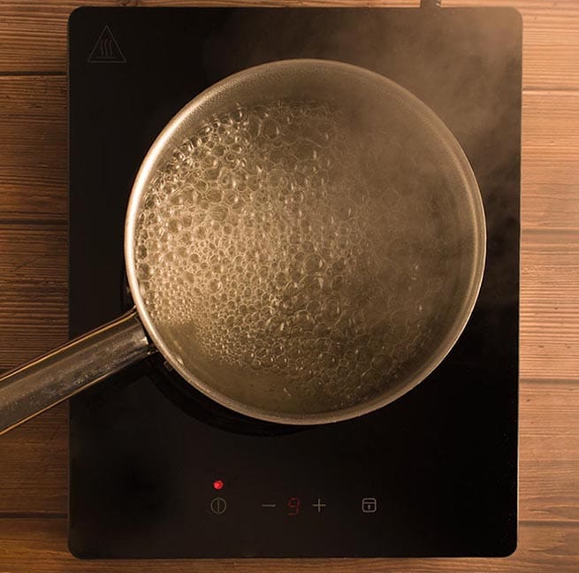 L'eau bout avec le sucre granulé blanc dans une petite casserole en stainless pour faire le sirop simple