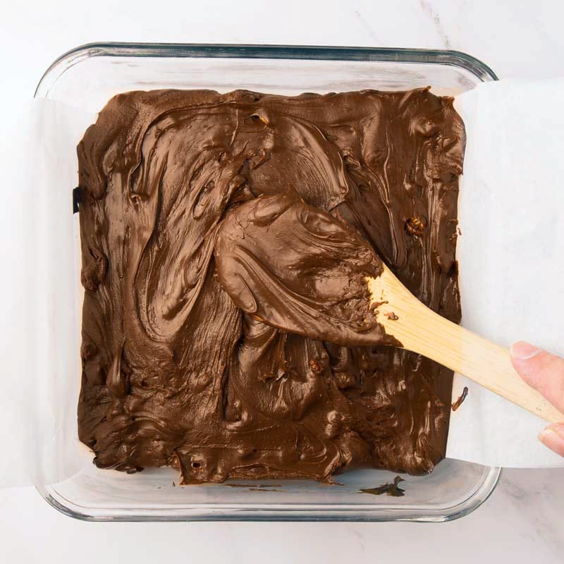 Le fudge est étendu dans le moule tapissé de papier parchemin et lissé avec le dos de la cuillère en bois avant la réfrigération