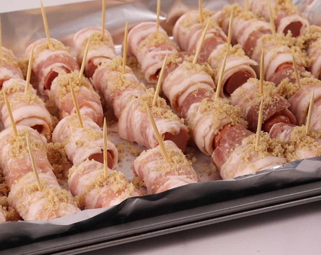 saucisses enrobees de bacon et parsemées de cassonade avant cuisson au four