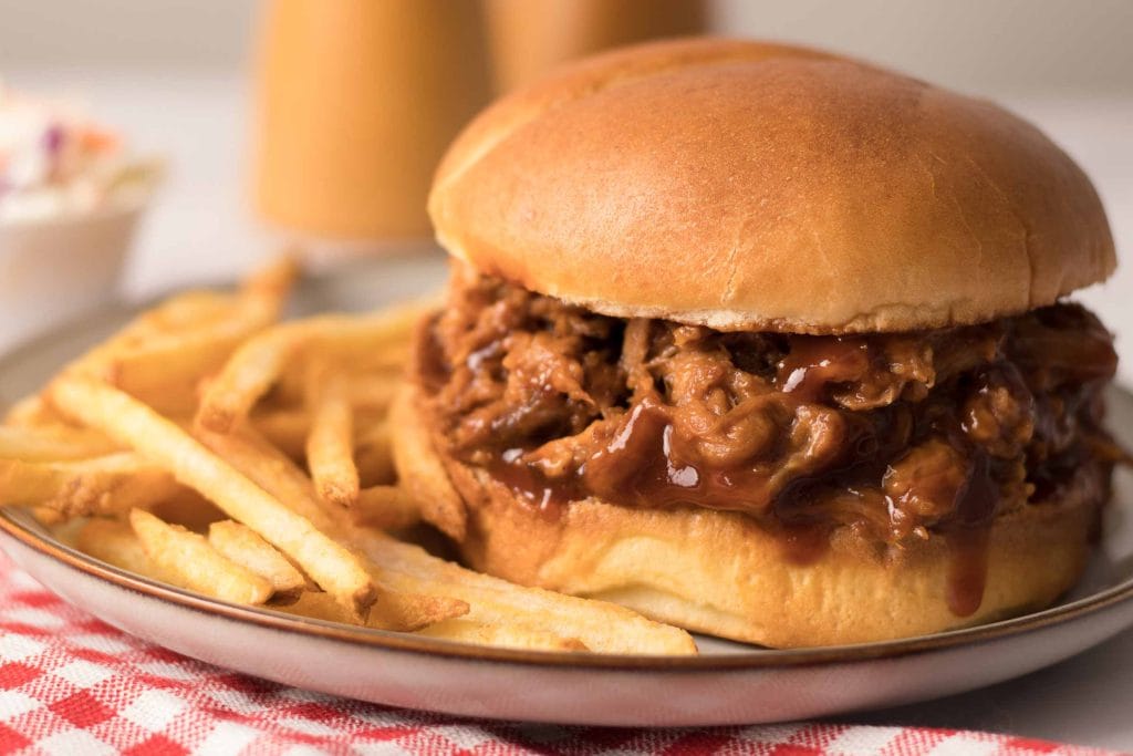 Porc effiloché tendre et juteux servi dans un pain hamburger grillé et accompagné de pommes de terre frites