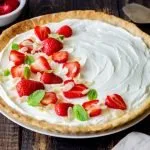 Tarte aux fraises garni de d'une crème fouettée au fromage à la crème et de morceaux de fraises, d'amandes effilées et de feuilles de menthe pour la décoration.