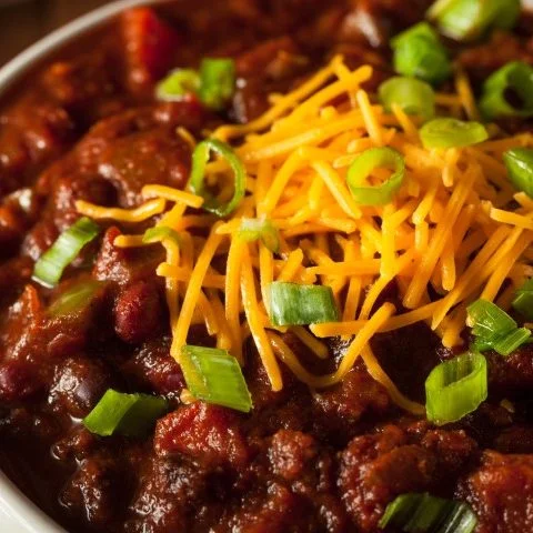 Bol de chili cuit à la mijoteuse servi avec fromage tex-mex râpé et des échalotes