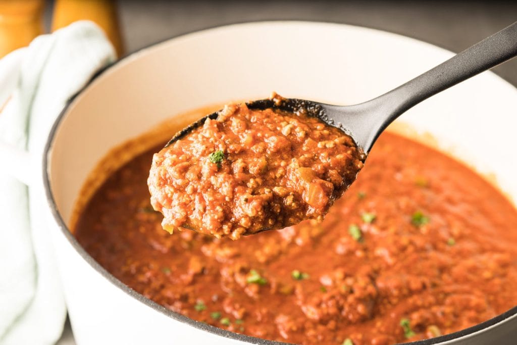 Cuillère remplie de sauce à spaghetti au dessus du chaudron de sauce qui a mijoté longtemps