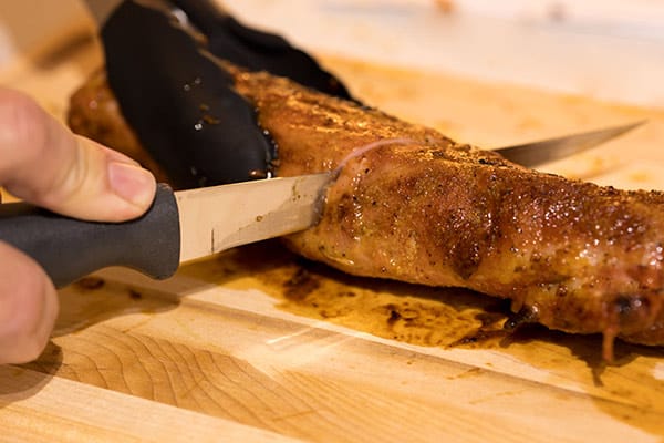 filet de porc tenu avec des pinces et coupé avec un couteau