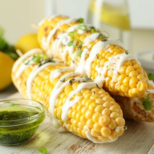 Trois épis de maïs avec crème sure et pesto servis sur une planche de bois
