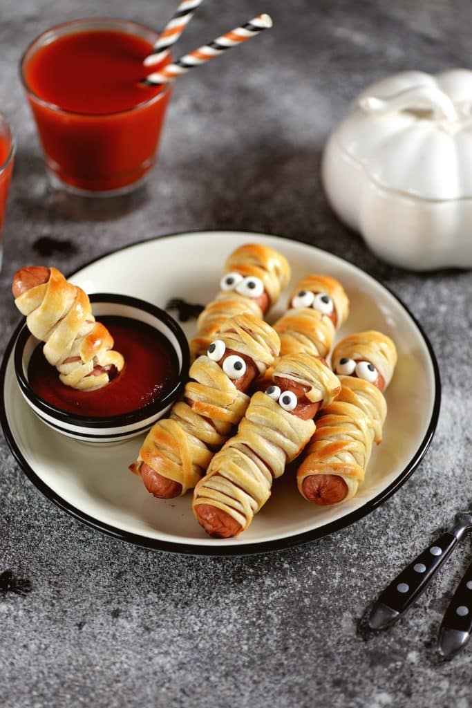 Saucisses momies servies sur une assiette avec une trempette de ketchup pour l'Halloween