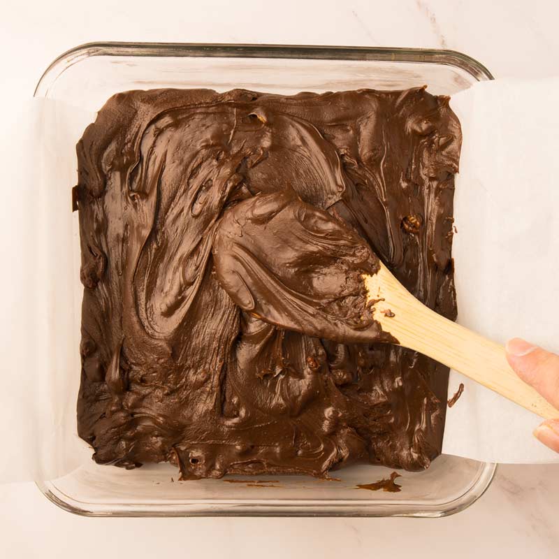 Le fudge est étendu dans le moule tapissé de papier parchemin et lissé avec le dos de la cuillère en bois avant la réfrigération