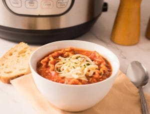 Bol de soupe à la lasagne garni de fromage mozzarella râpé et accompagné de pain.