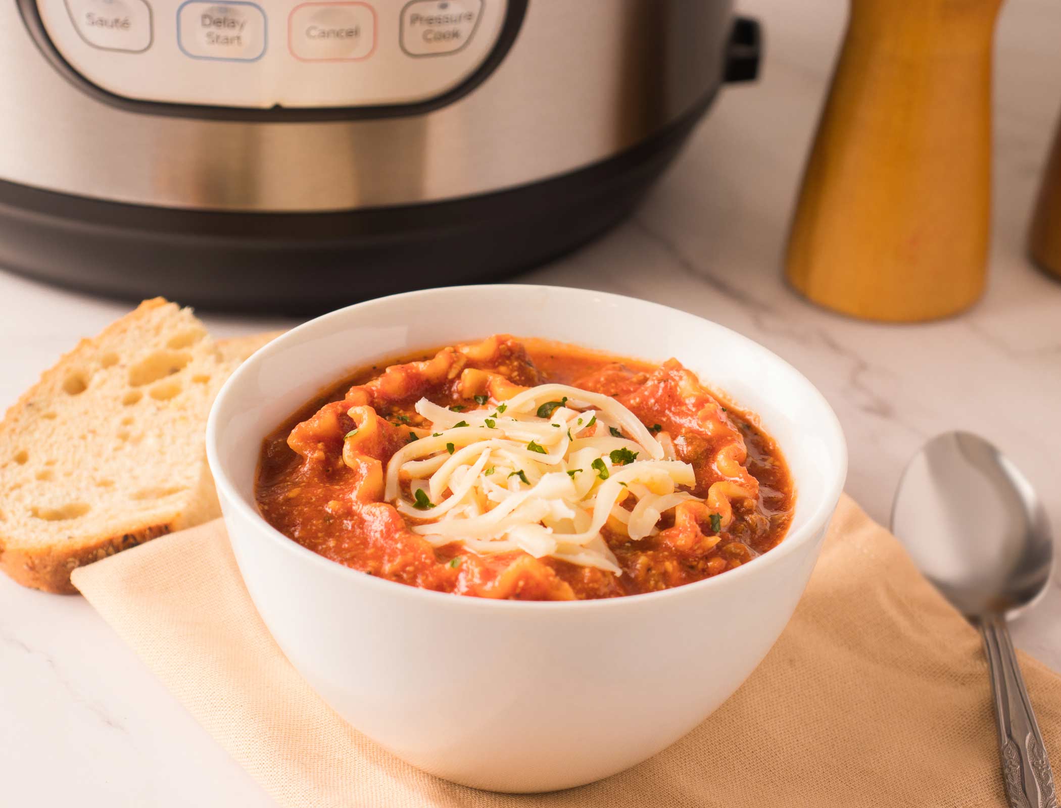 Bol de soupe à la lasagne garni de fromage mozzarella râpé et accompagné de pain.