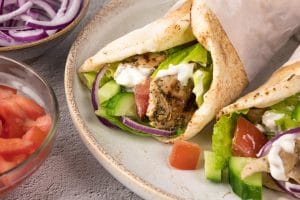 Un gyro au poulet grec avec garnitures de tomates, oignons rouges, concombre, laitue et sauce tzatziki dans un pain pita