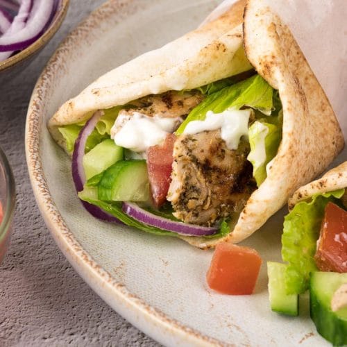 Un gyro au poulet grec avec garnitures de tomates, oignons rouges, concombre, laitue et sauce tzatziki dans un pain pita